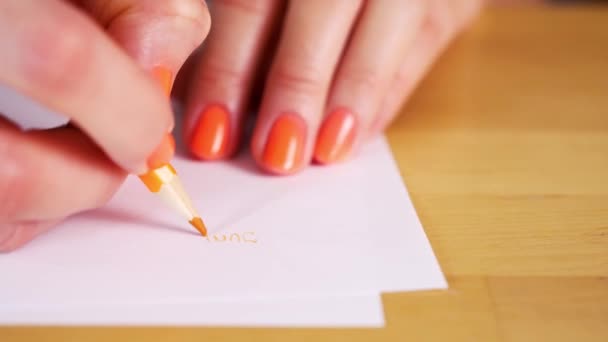 Vrouw houdt een oranje potlood vast en maakt aantekeningen op een wit papier — Stockvideo