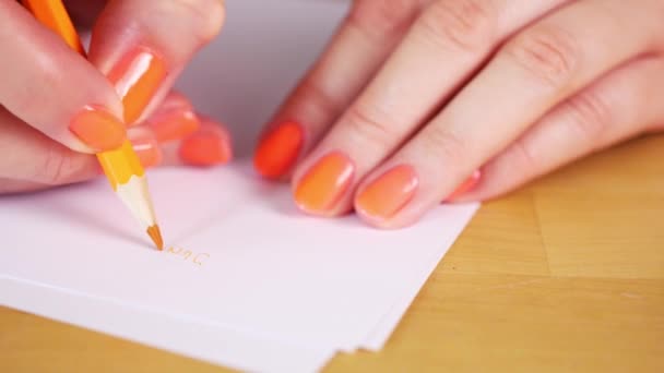 femme tient un crayon orange et prend des notes sur un papier blanc 