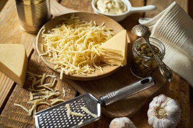 Mutfak masasında peynir rendesi ve kapari ve fesleğen ile rendelenmiş sarı peynir