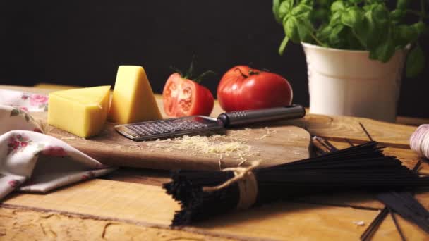 Подрібнений сир зі свіжим базиліком та італійським спагетті на дерев'яному кухонному столі — стокове відео