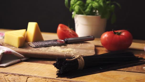Geschredderter Käse mit frischem Basilikum und italienischen Spaghetti auf hölzernem Küchentisch — Stockvideo