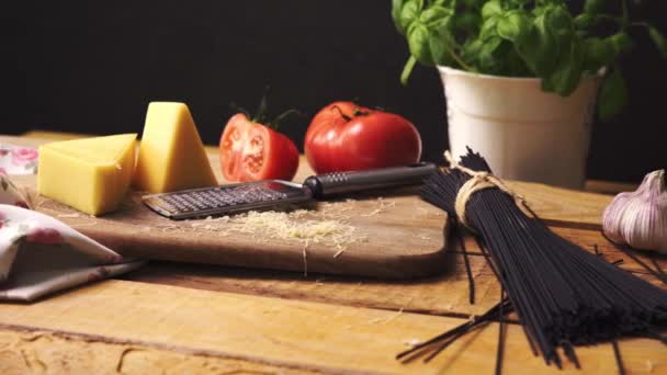 Измельченный сыр со свежим базиликом и итальянскими спагетти на деревянном кухонном столе — стоковое видео