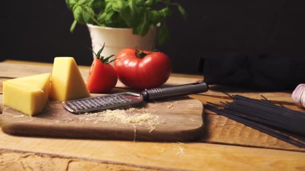 Τριμμένο τυρί με φρέσκο βασιλικό και ιταλικό σπαγγέτι σε ξύλινο τραπέζι κουζίνας — Αρχείο Βίντεο
