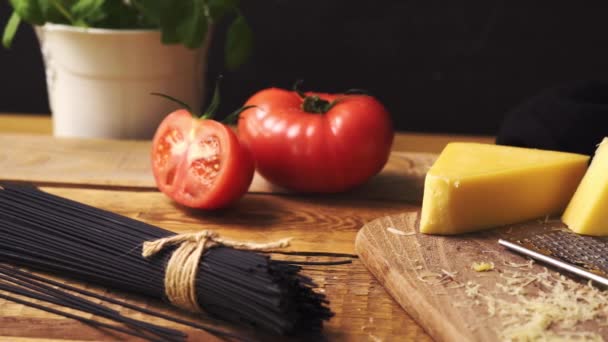 Shredded cheese with fresh basil and italian spaghetti on wooden kitchen table — Stock Video