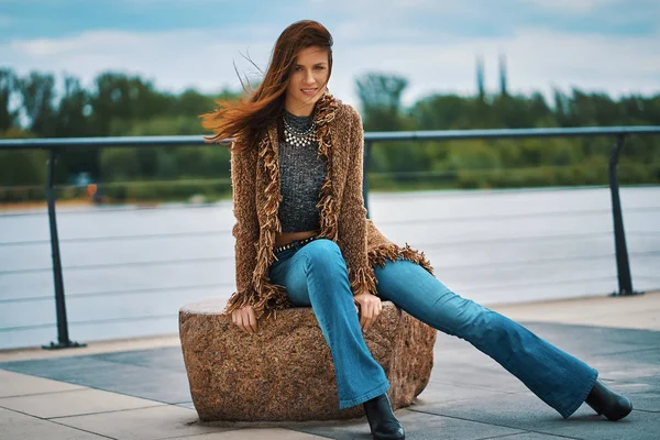Красивая молодая женщина позирует на каменной скамейке на набережной у реки в городе — стоковое фото