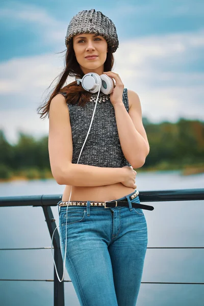 Beautiful woman with white earphones posing on the promenade by the river in the city
