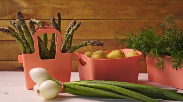 Verduras jóvenes de primavera en contenedores de coral sobre mesa de madera — Vídeo de stock