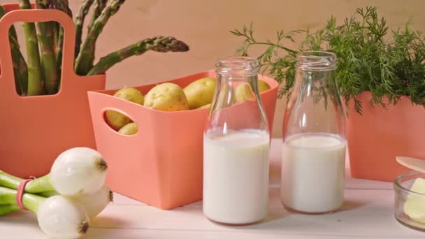 Άνοιξη νεαρά λαχανικά σε δοχεία κοραλλιών και μπουκάλια με γάλα στο τραπέζι — Αρχείο Βίντεο