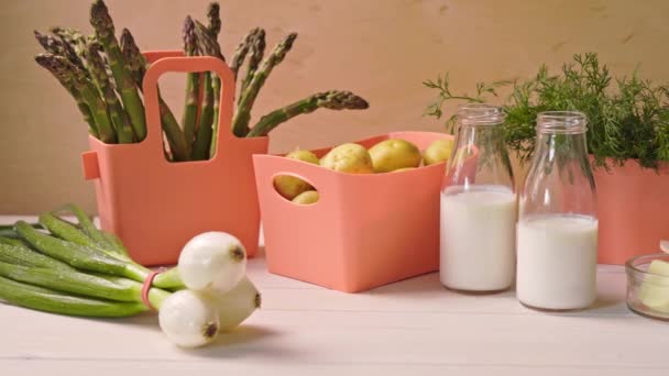 Frühjahrsjunges Gemüse in Korallenbehältern und Flaschen mit Milch auf dem Tisch — Stockvideo
