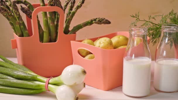 Verduras jóvenes de primavera en contenedores de coral y botellas con leche sobre la mesa — Vídeo de stock