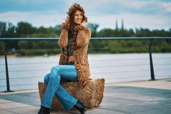 Красивая молодая женщина позирует на каменной скамейке на набережной у реки в городе — стоковое фото