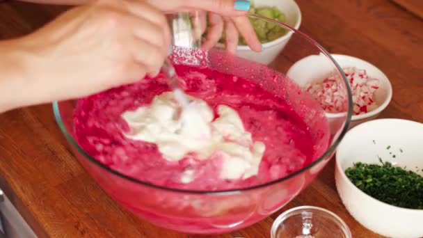 Woman prepares cold beetroot soup in glass bowl on wooden table — Stock Video