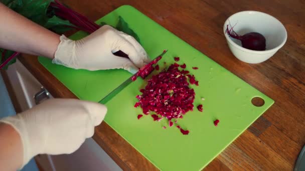 Вид женских рук в перчатках, разрезающих свеклу на деревянном столе — стоковое видео