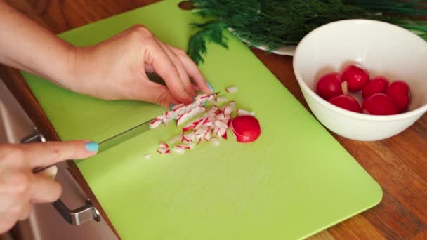 Mulher está cortando rabanete fresco na cozinha na mesa de madeira — Vídeo de Stock