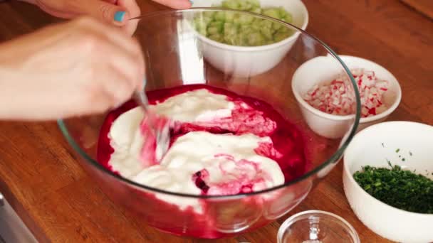 Woman prepares cold beetroot soup in glass bowl on wooden table — Stock Video