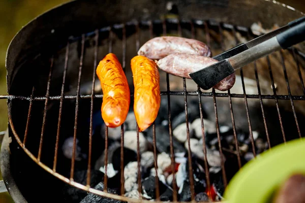 Saftig korv på varm grill med tång under sommaren grill — Stockfoto