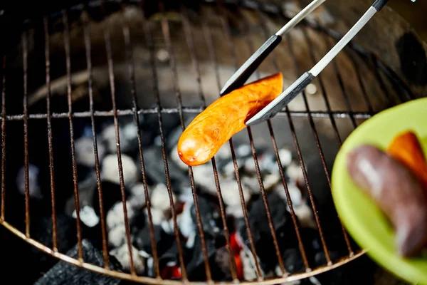 Salsicha suculenta na grelha quente com pinças durante o churrasco de verão — Fotografia de Stock