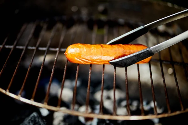 Saftige Wurst auf heißem Grill mit Zange beim Sommergrillen — Stockfoto