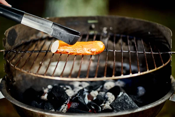 Salsicha suculenta na grelha quente com pinças durante o churrasco de verão — Fotografia de Stock