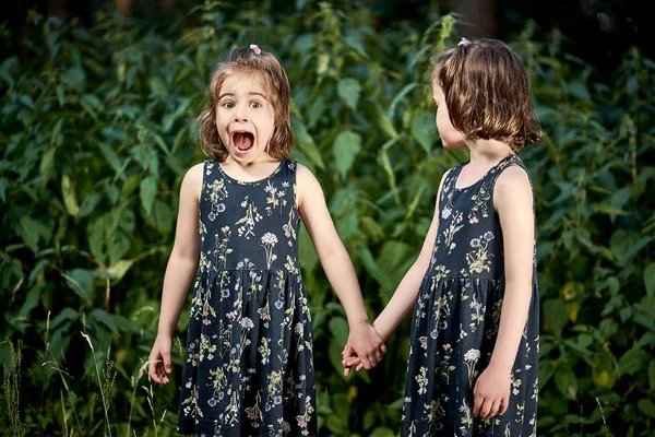 Beautiful little girls are afraid of nettles in forest on summer day