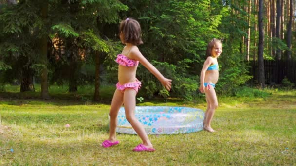 Dua gadis kecil bermain dengan balon air oleh kolam renang pada waktu musim panas — Stok Video