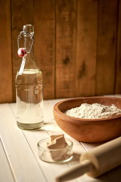 Top view of bowl of flour with yeast and rolling pin on  white  kitchen table