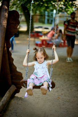 Oyun üzerinde dalgın yüz ile salıncak üzerinde küçük güzel üzgün kız