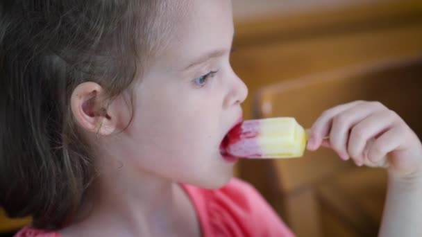 Mooi klein meisje dat een heerlijk kleurrijk ijsje eet — Stockvideo