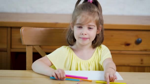 Meisje in een gele jurk met krijtjes trekt op papier — Stockvideo