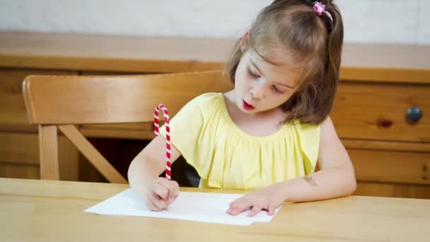 Liten flicka i en gul klänning med en penna ritar på papper — Stockvideo