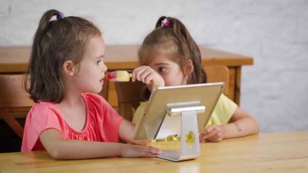 Dos niñas comen helado y ven dibujos animados en la tableta — Vídeo de stock