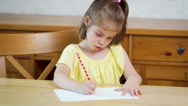 Маленька дівчинка в жовтій сукні з олівцем малює на папері — стокове відео