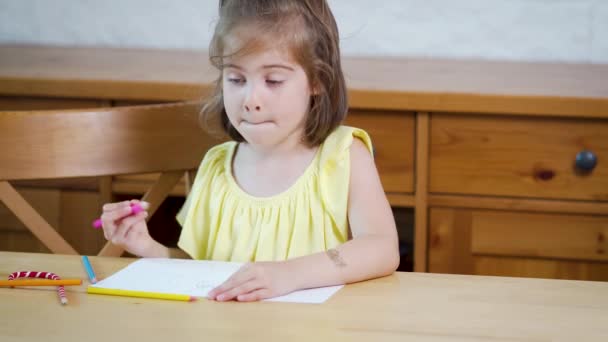 Niña en un vestido amarillo con lápices de colores dibuja sobre papel — Vídeo de stock