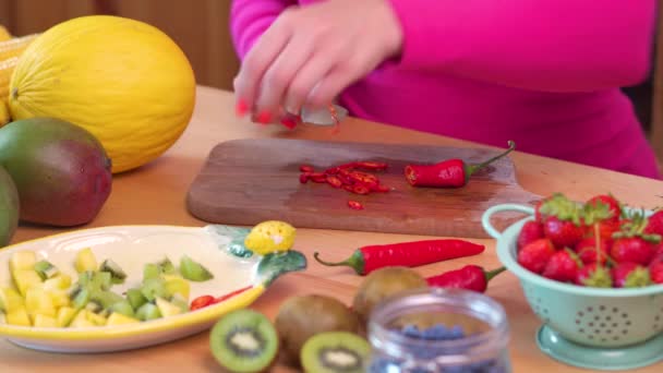 Frau in rosa Bluse schneidet würzige rote Chilischoten auf einem Tisch — Stockvideo