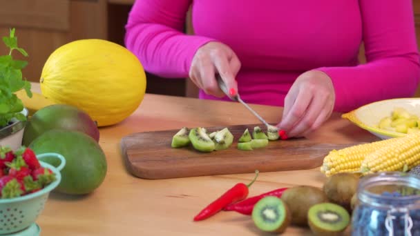 Frau in rosa Bluse schneidet saftige grüne Kiwi — Stockvideo