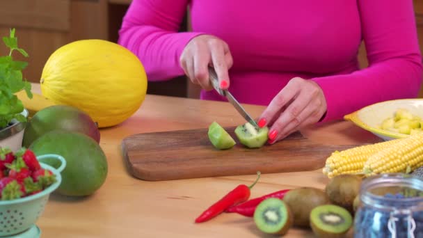 Mulher em uma blusa rosa cortando kiwi verde suculento em uma mesa — Vídeo de Stock