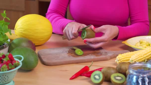 Vrouw in een roze blouse hakken sappige groene kiwi — Stockvideo