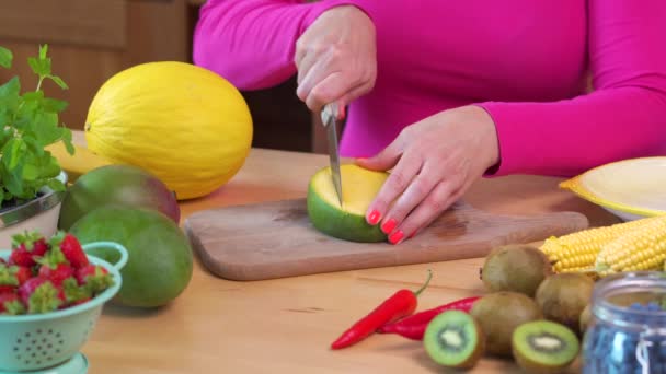 Mujer en una blusa rosa cortando un jugoso mango amarillo sobre una mesa — Vídeos de Stock