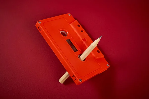 어두운 빨간색 배경에 오렌지 오디오 카세트와 연필 — 스톡 사진
