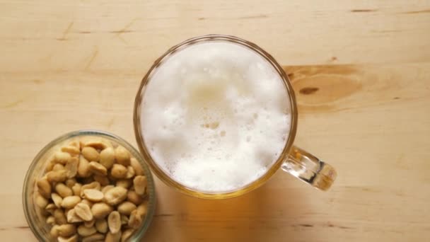 Top zicht op bier met schuim en zoute pinda's en op houten tafel — Stockvideo