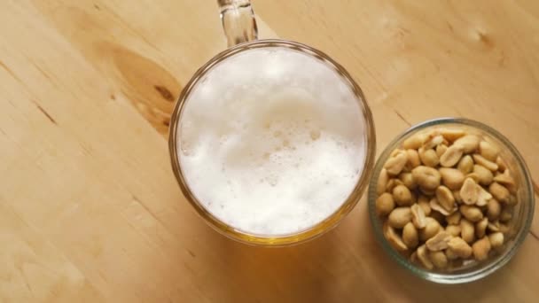 Вид зверху на пиво з піною і солоними горіхами і на дерев'яний стіл — стокове відео