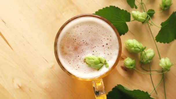 Top view of mug of beer with foam and hops on bright wooden table — Stock Video