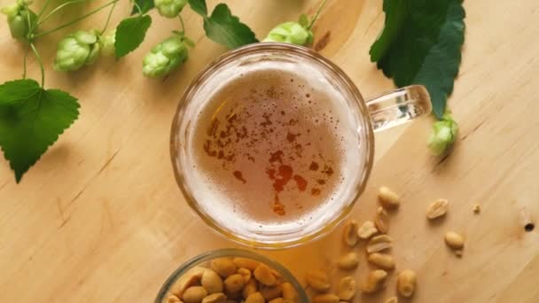 Vista superior de la cerveza con espuma y cacahuetes salados y sobre mesa de madera — Vídeos de Stock