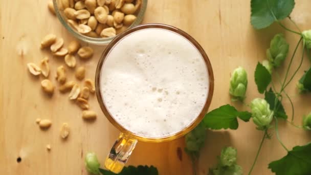 Top view of beer with foam and salty peanuts and on wooden table — Stock Video