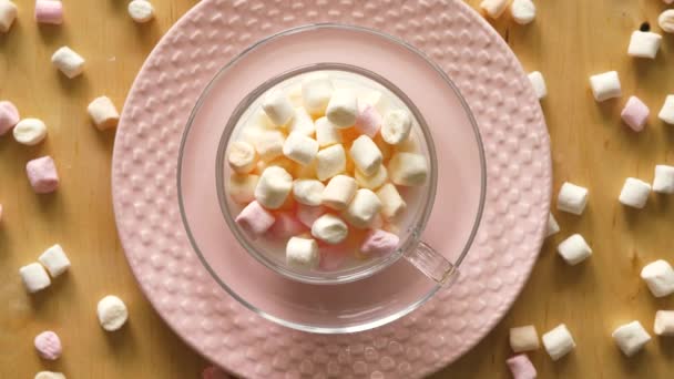 Vista superior no copo com marshmallows na placa rosa e mesa de madeira — Vídeo de Stock