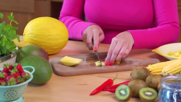 Vrouw in een roze blouse hakken een sappige gele mango — Stockvideo