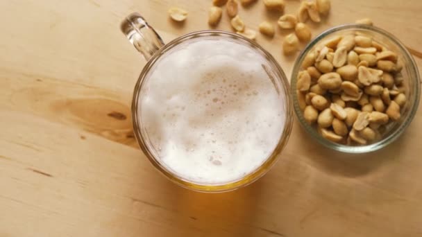 Vista superior de la cerveza con espuma y cacahuetes salados y sobre mesa de madera — Vídeos de Stock