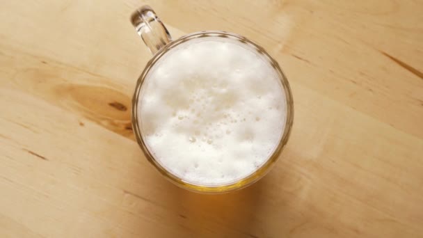 Вид сверху на бутылку светлого пива с пеной на деревянном столе — стоковое видео