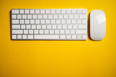 Sarı masa üzerinde beyaz bilgisayar klavyesi ve fare üst görünümü