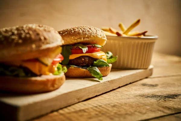 Dos sabrosas hamburguesas y papas fritas sobre tabla de madera y fondo negro — Foto de Stock